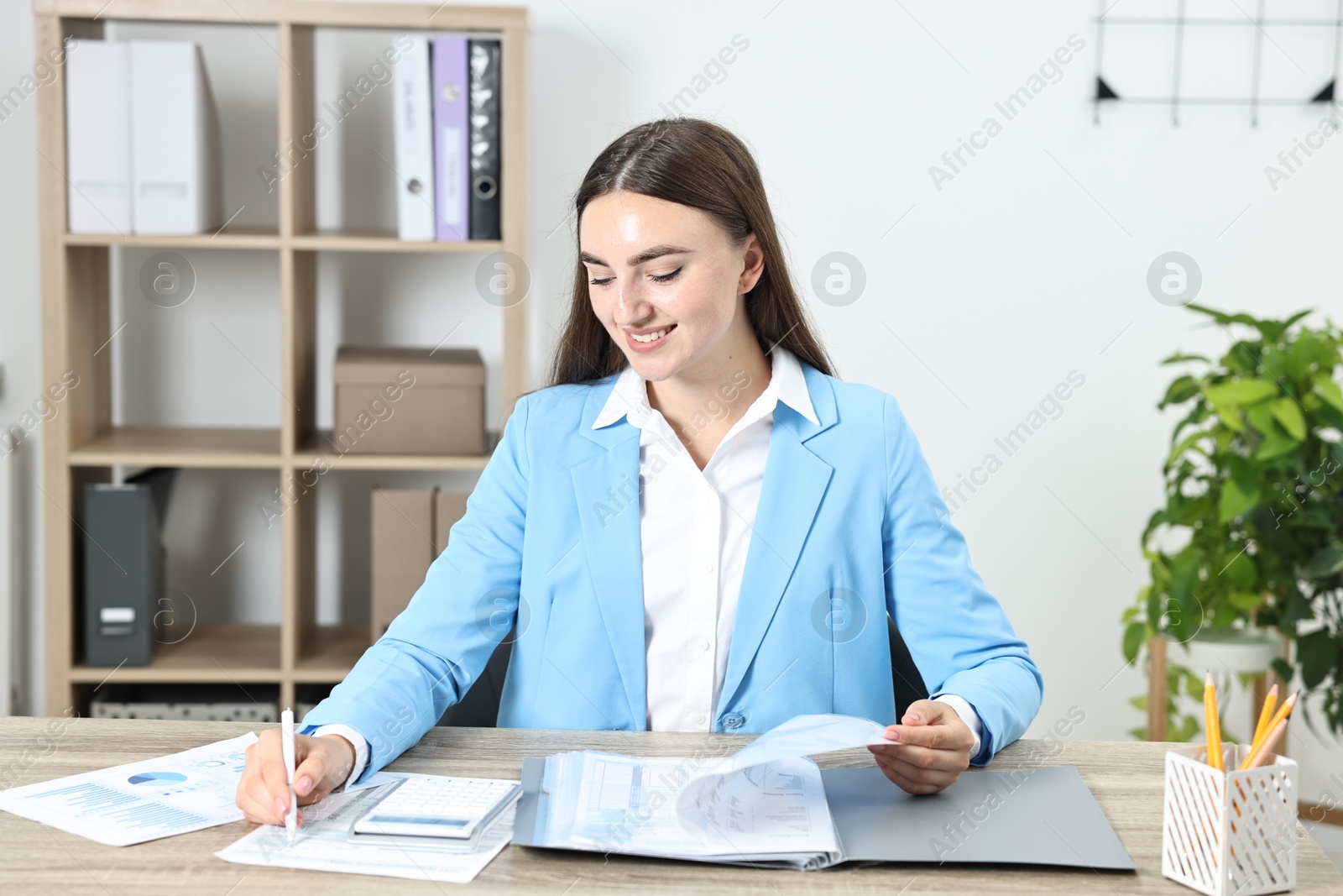 Photo of Budget planning. Beautiful young woman with papers and calculator at wooden table in office