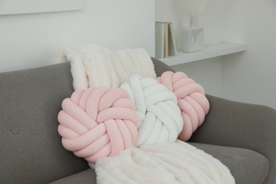 Different soft pillows in shape of knot and blanket on sofa in room