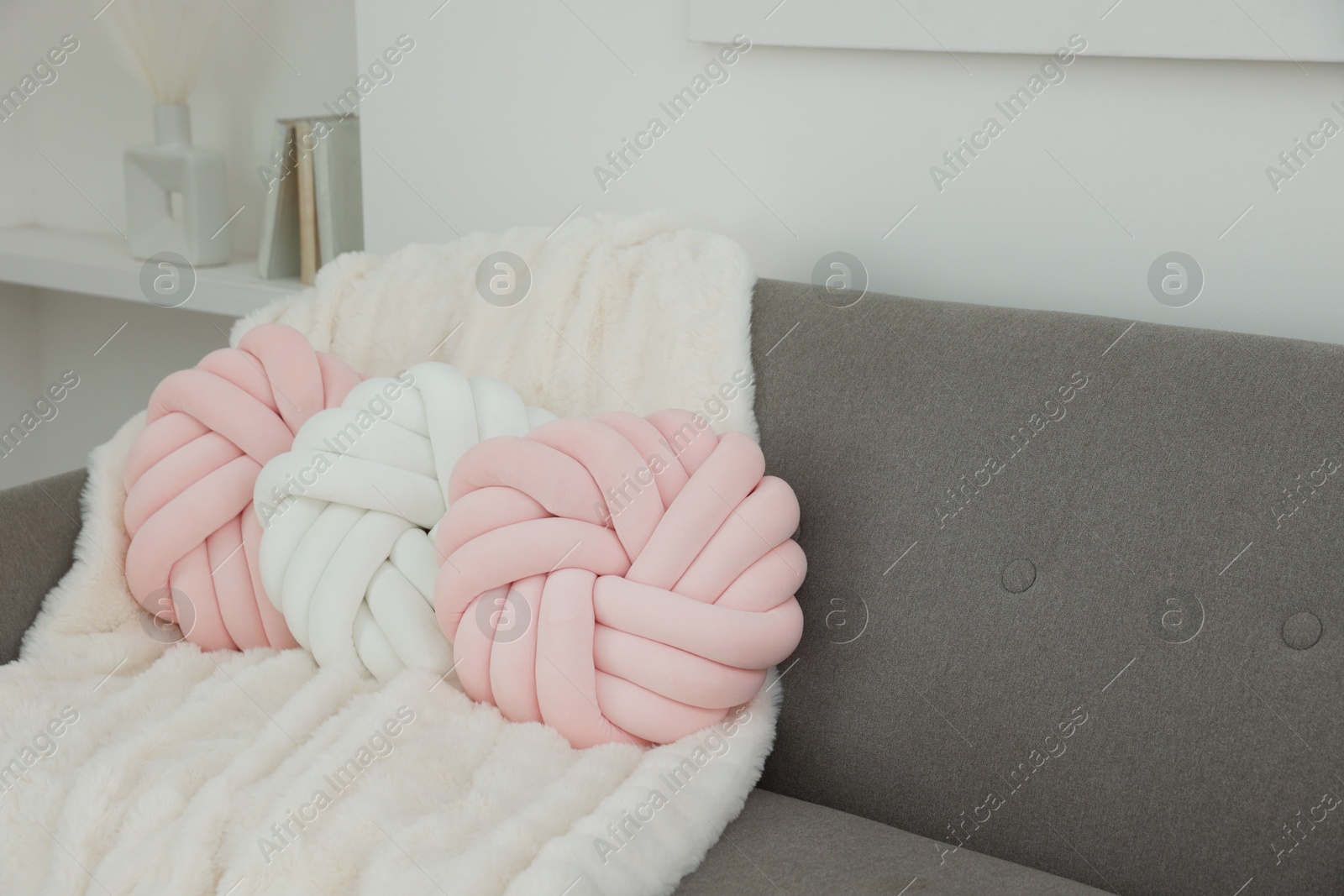 Photo of Different soft pillows in shape of knot and blanket on sofa in room