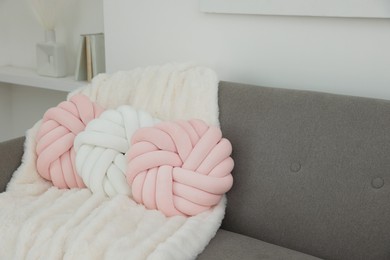 Photo of Different soft pillows in shape of knot and blanket on sofa in room