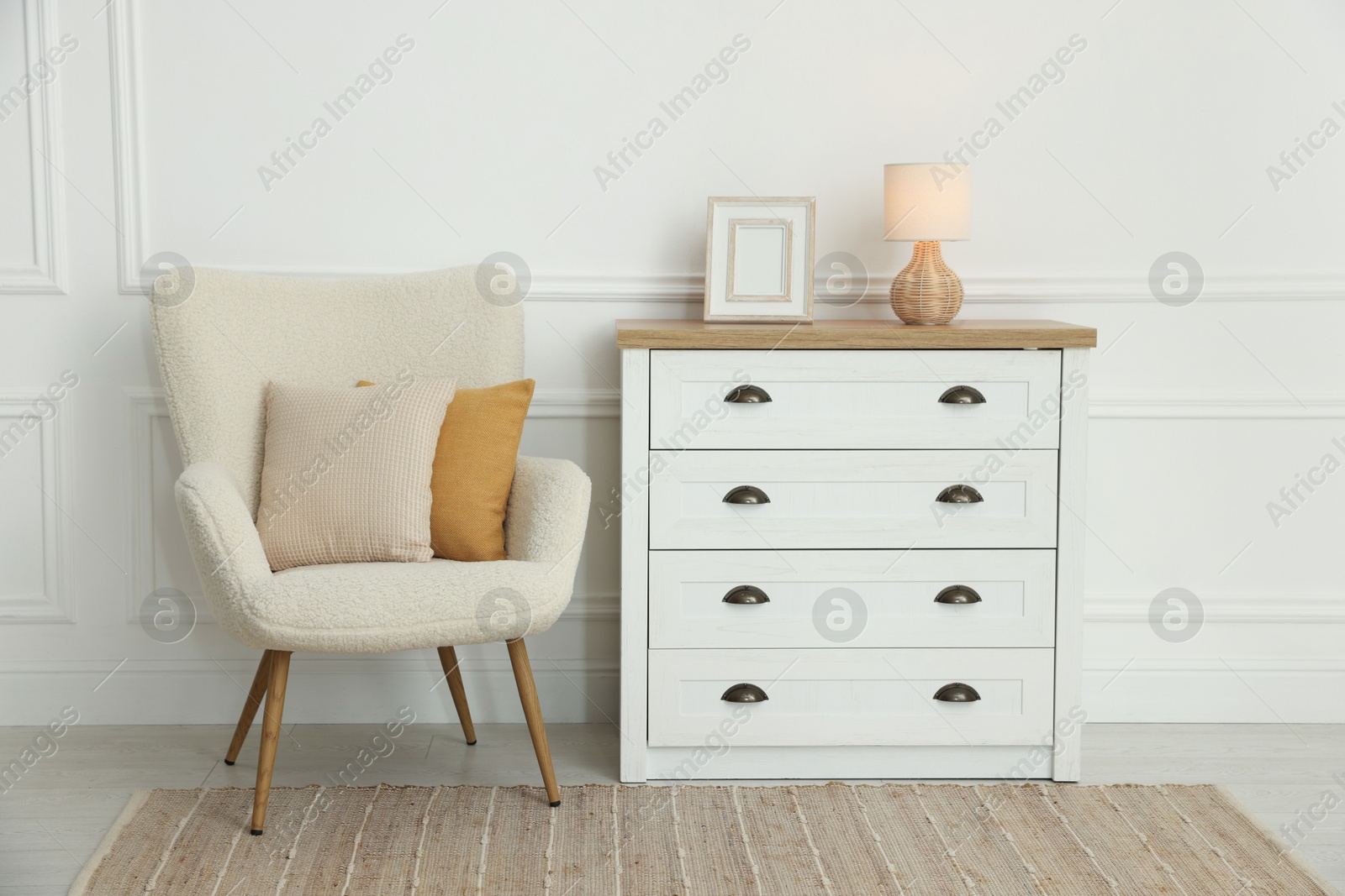 Photo of Soft pillows on armchair and chest of drawers indoors