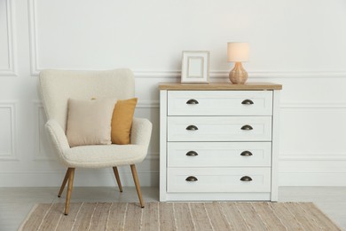 Photo of Soft pillows on armchair and chest of drawers indoors