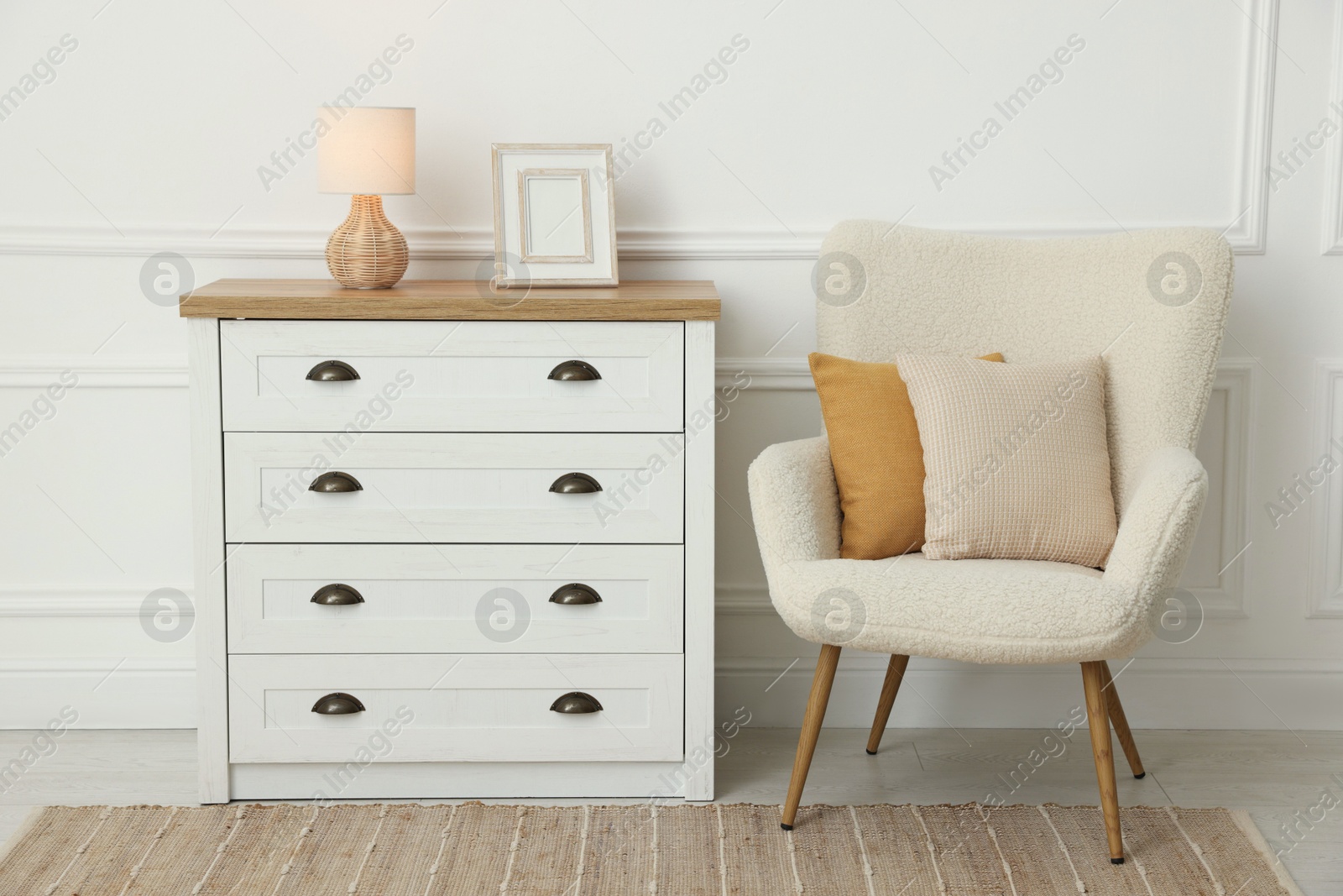 Photo of Soft pillows on armchair and chest of drawers indoors