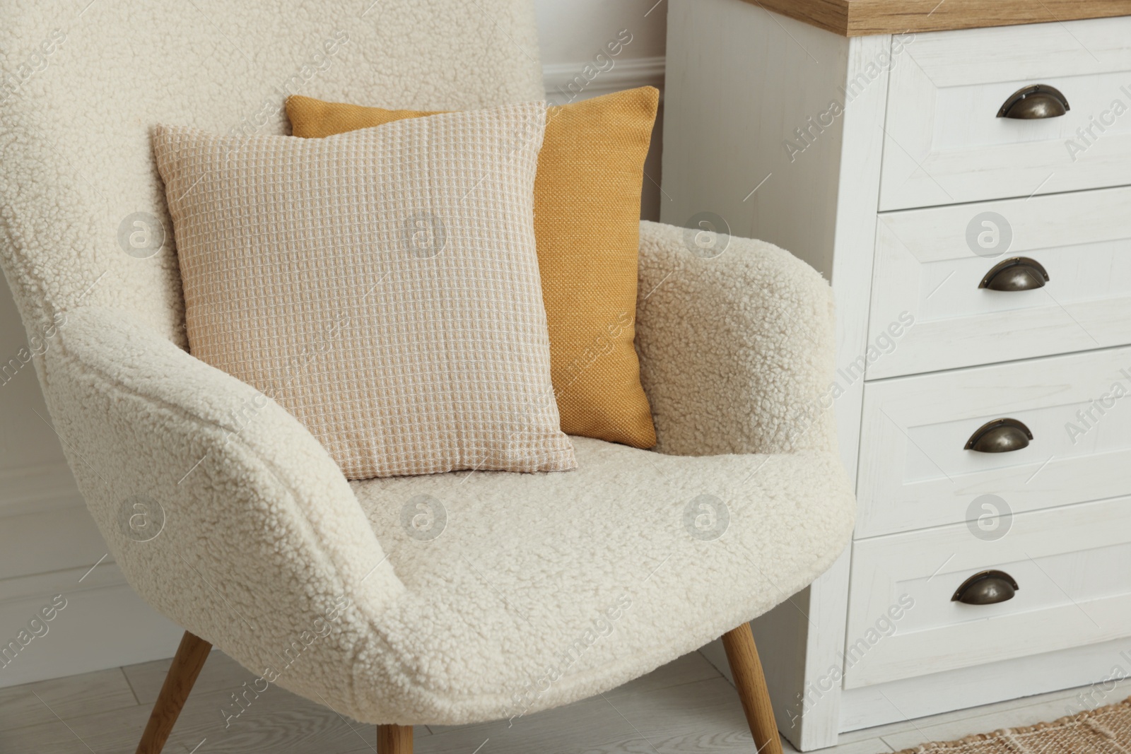 Photo of Soft pillows on armchair and chest of drawers indoors