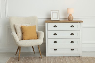 Photo of Soft pillows on armchair and chest of drawers indoors