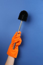 Photo of Woman holding black toilet brush on blue background, closeup. Cleaning tool