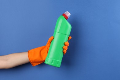 Photo of Woman holding toilet cleaner in bottle on blue background, closeup