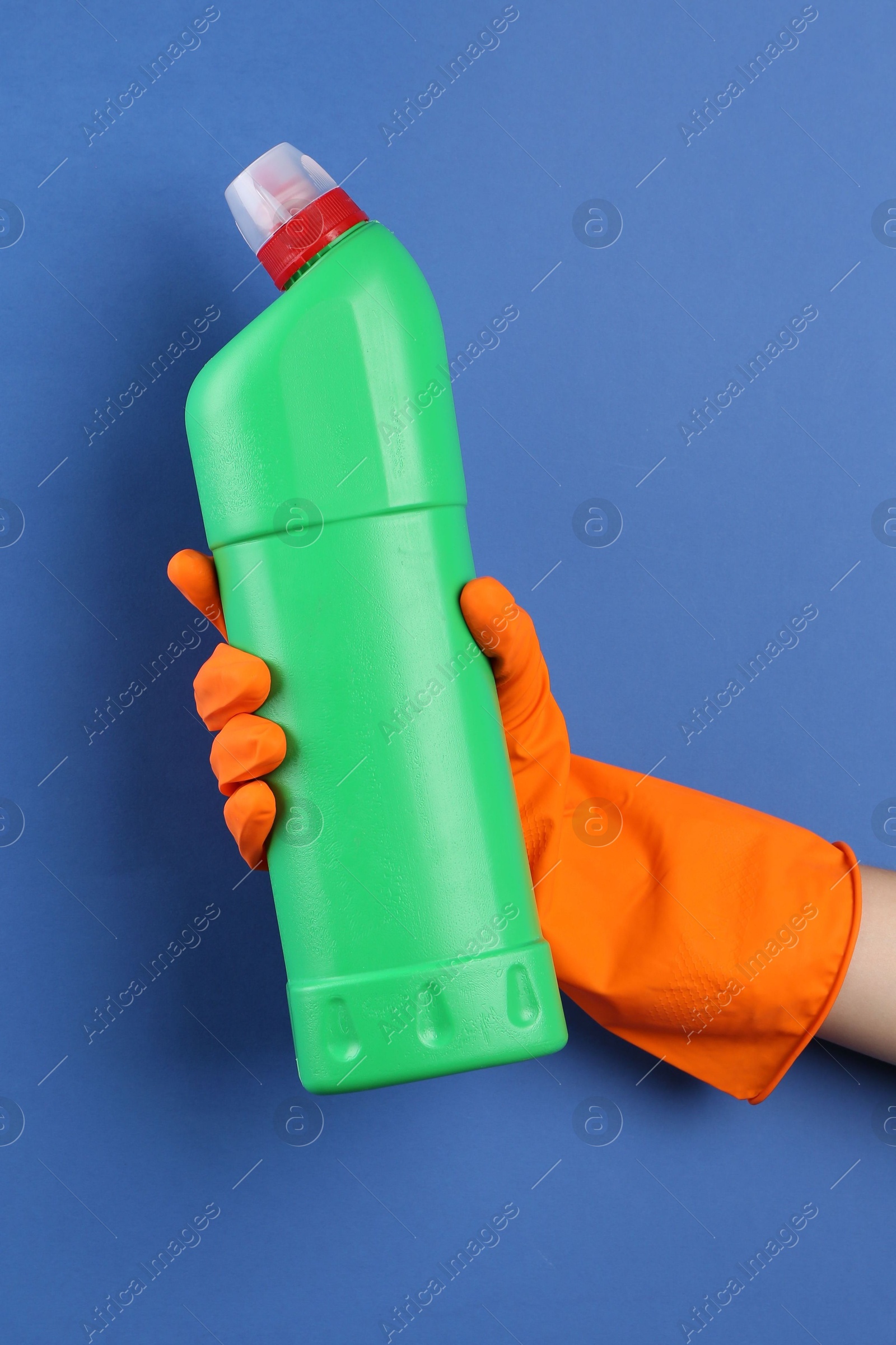 Photo of Woman holding toilet cleaner in bottle on blue background, closeup