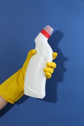 Photo of Woman holding toilet cleaner in bottle on blue background, closeup