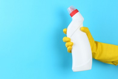 Photo of Woman holding toilet cleaner in bottle on light blue background, closeup. Space for text