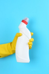 Photo of Woman holding toilet cleaner in bottle on light blue background, closeup