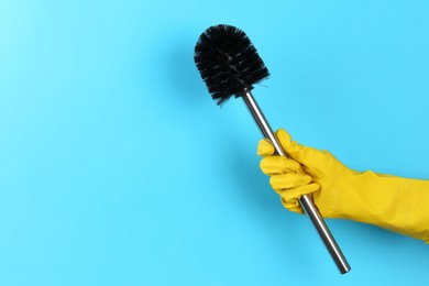 Photo of Woman holding black toilet brush on light blue background, closeup. Space for text