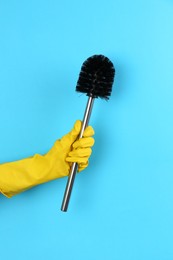 Photo of Woman holding black toilet brush on light blue background, closeup. Cleaning tool