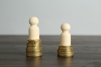 Photo of Financial inequality. Human figures and coins on wooden table