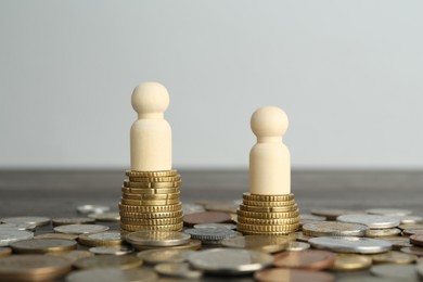 Photo of Financial inequality. Human figures and coins on wooden table