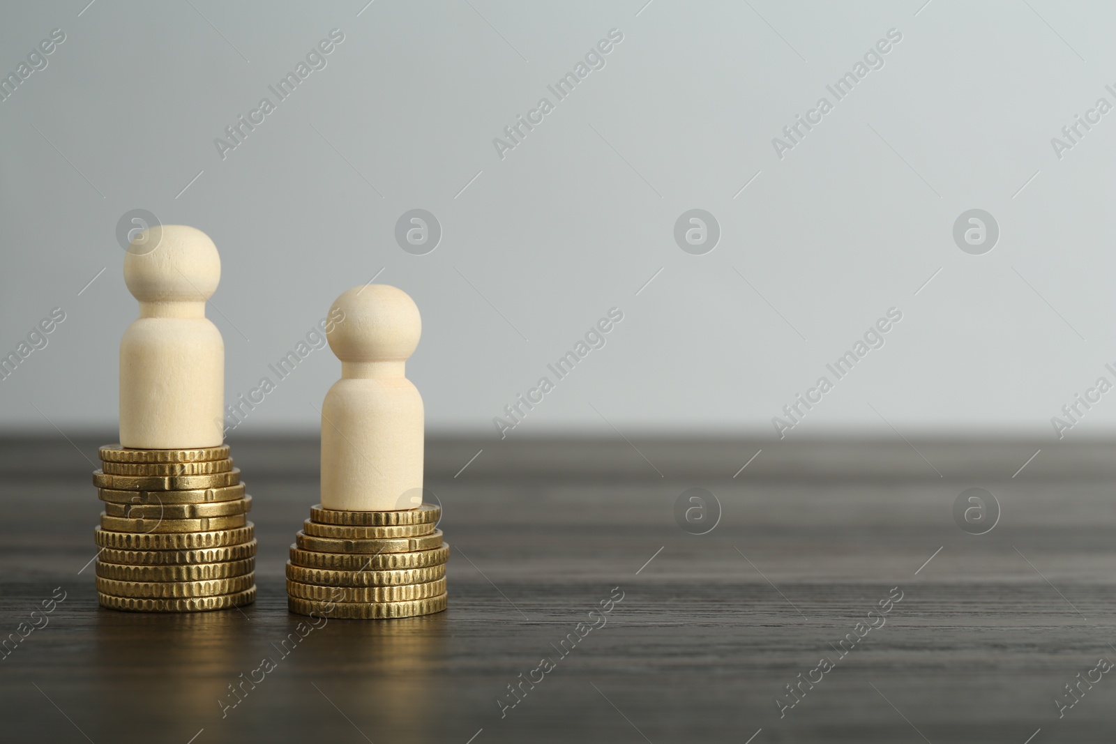 Photo of Financial inequality. Human figures and coins on wooden table. Space for text