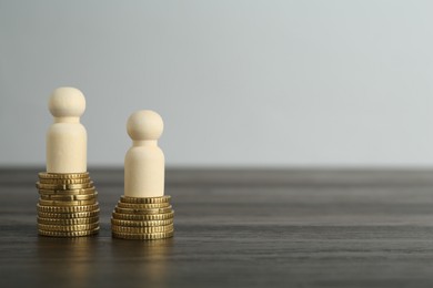 Photo of Financial inequality. Human figures and coins on wooden table. Space for text