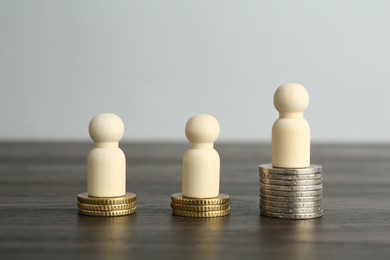 Photo of Financial inequality. Human figures and coins on wooden table