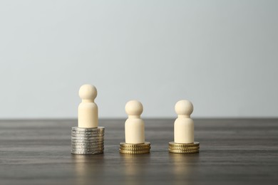 Photo of Financial inequality. Human figures and coins on wooden table