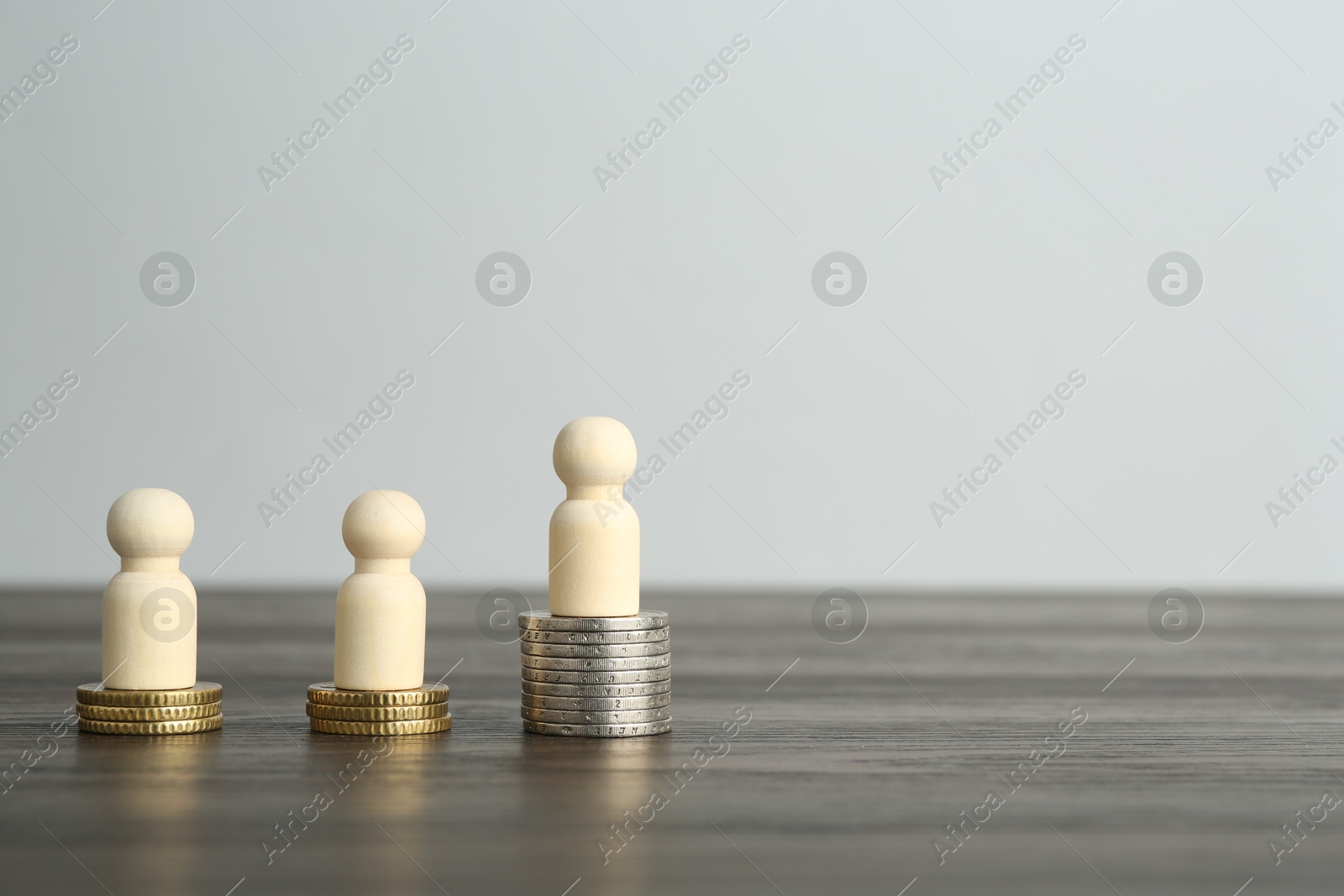 Photo of Financial inequality. Human figures and coins on wooden table. Space for text