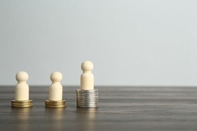 Photo of Financial inequality. Human figures and coins on wooden table. Space for text