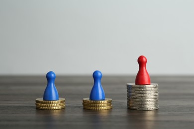 Photo of Financial inequality. Human figures and coins on wooden table