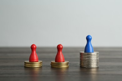 Photo of Financial inequality. Human figures and coins on wooden table