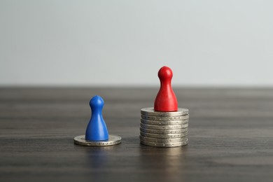 Photo of Financial inequality. Human figures and coins on wooden table