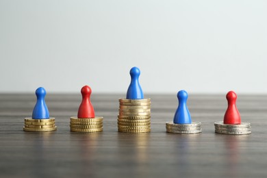 Photo of Financial inequality. Human figures and coins on wooden table