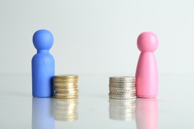 Photo of Financial inequality. Male and female figures with coins on light table