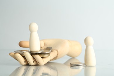 Photo of Financial inequality. Human figures, coins and wooden hand on light table