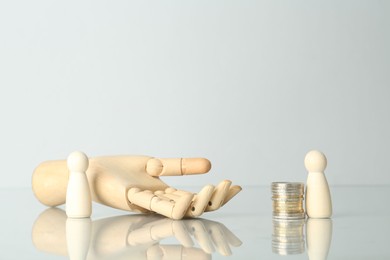 Photo of Financial inequality. Human figures, coins and wooden hand on light table