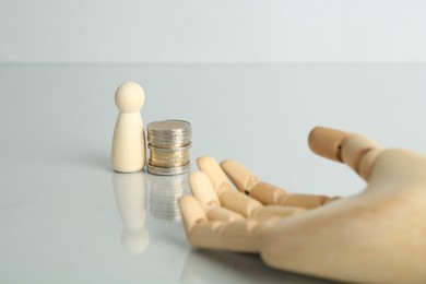 Photo of Financial inequality. Human figure, coins and wooden hand on light table