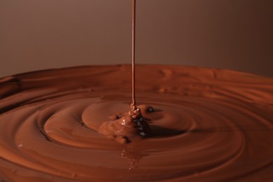 Photo of Pouring delicious melted chocolate on brown background, closeup