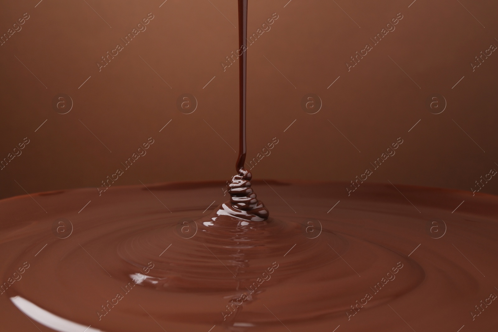 Photo of Pouring delicious melted chocolate on brown background, closeup