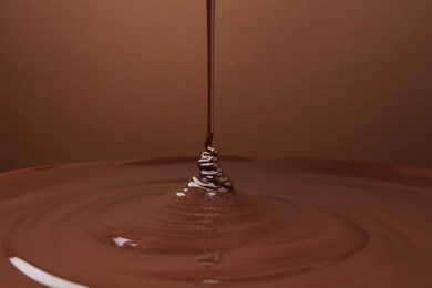 Photo of Pouring delicious melted chocolate on brown background, closeup