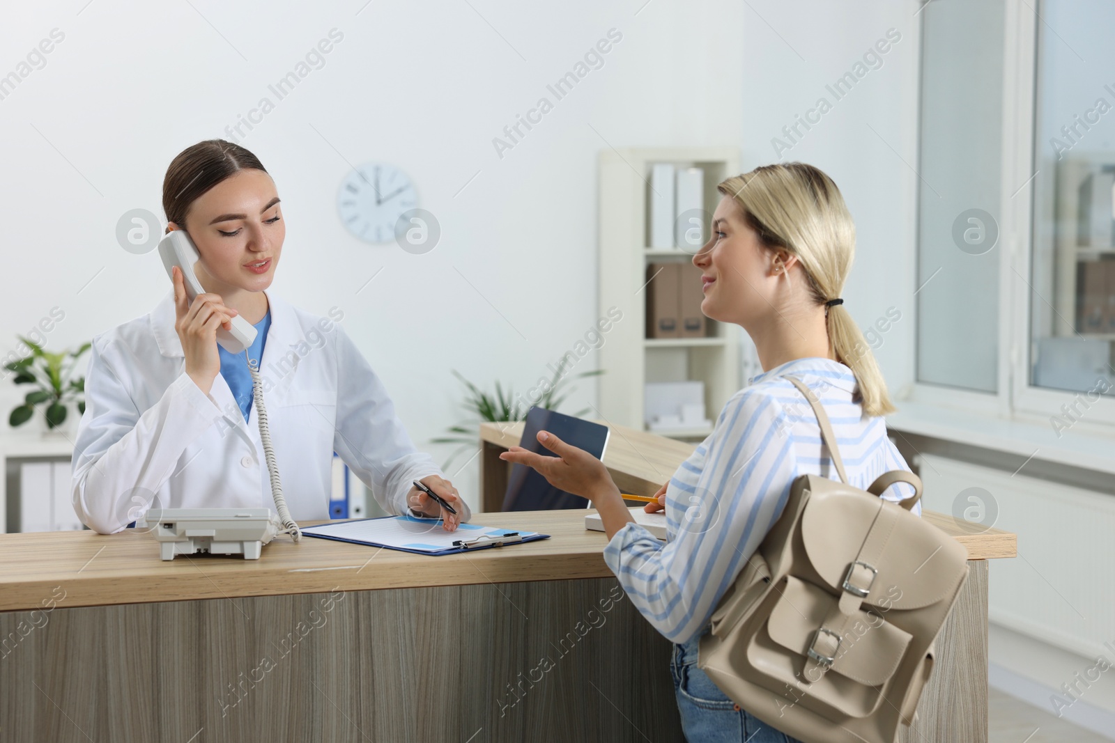 Photo of Professional receptionist working with patient at wooden desk in hospital