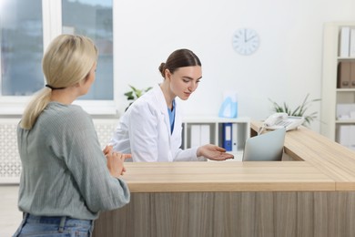 Photo of Professional receptionist working with patient at wooden desk in hospital