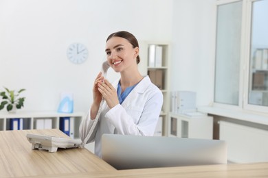 Photo of Professional receptionist talking on phone at wooden desk in hospital