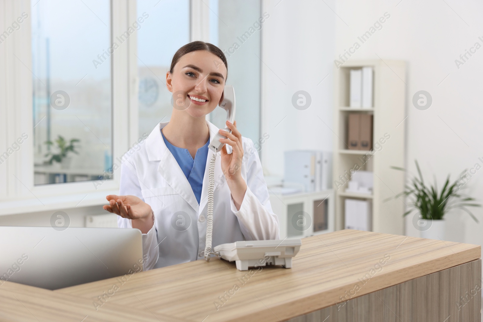 Photo of Professional receptionist talking on phone at wooden desk in hospital