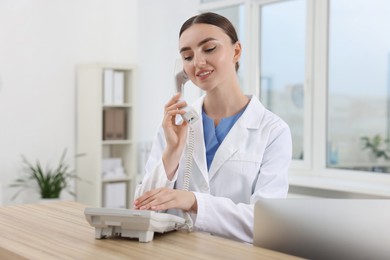 Professional receptionist talking on phone at wooden desk in hospital