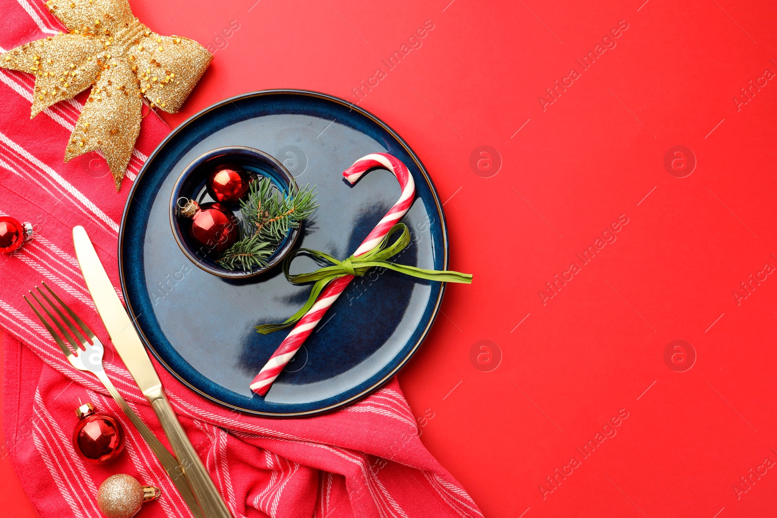 Photo of Beautiful Christmas setting with plate, elegant cutlery and festive decor on red table, flat lay. Space for text