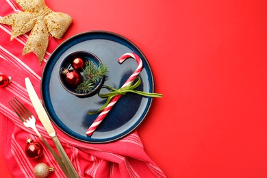 Photo of Beautiful Christmas setting with plate, elegant cutlery and festive decor on red table, flat lay. Space for text