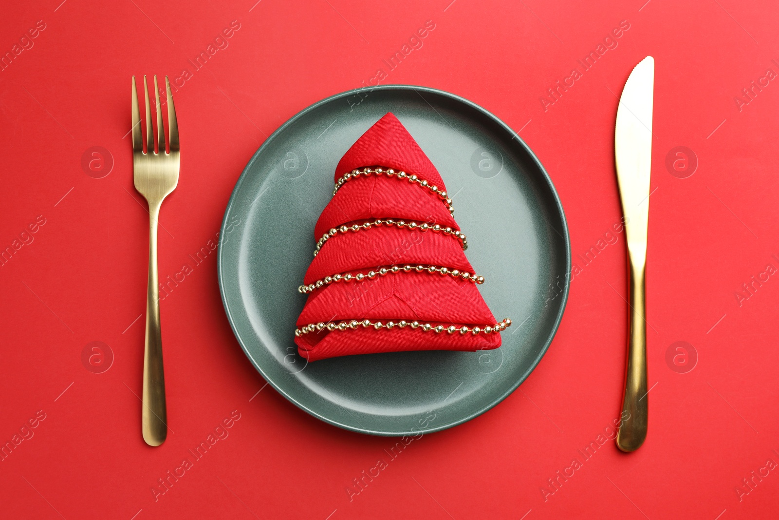 Photo of Beautiful Christmas setting with plate, elegant cutlery and festive decor on red table, flat lay