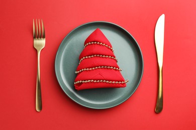 Photo of Beautiful Christmas setting with plate, elegant cutlery and festive decor on red table, flat lay