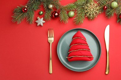 Photo of Beautiful Christmas setting with plate, elegant cutlery and festive decor on red table, flat lay