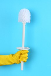 Photo of Woman holding white toilet brush on light blue background, closeup. Cleaning tool