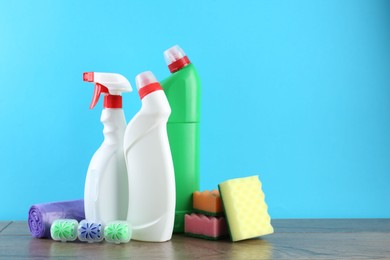 Photo of Different toilet cleaners, sponges and trash bags on wooden table against light blue background