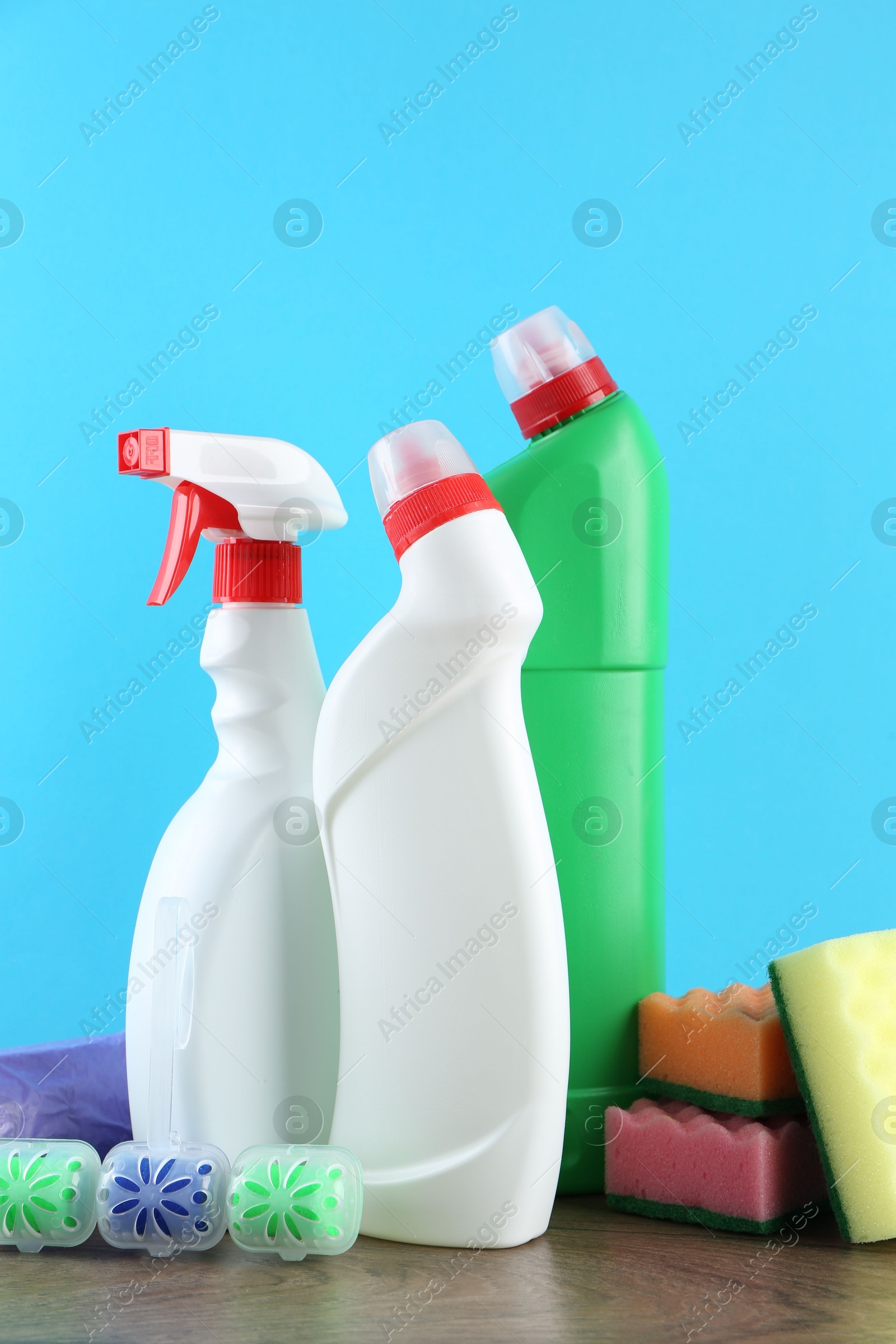 Photo of Different toilet cleaners, sponges and trash bags on wooden table against light blue background