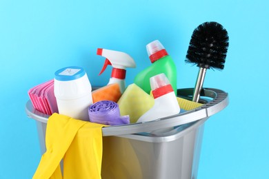 Photo of Bucket with different toilet cleaners, rags, rubber gloves and trash bags on light blue background